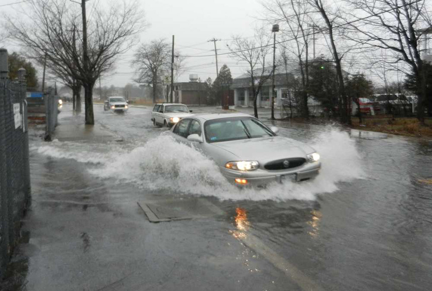 A car drives through a flooded main street with water reaching the top of the car