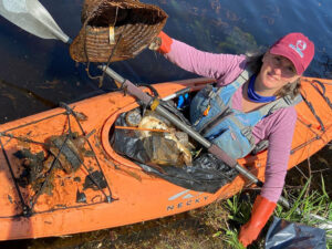 Volunteer in kayak cleaning nips from river